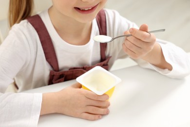 Photo of Cute little girl with tasty yogurt at white table, closeup