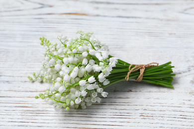 Photo of Beautiful lily of the valley flowers on white wooden table