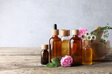 Aromatherapy. Different essential oils and flowers on wooden table, space for text