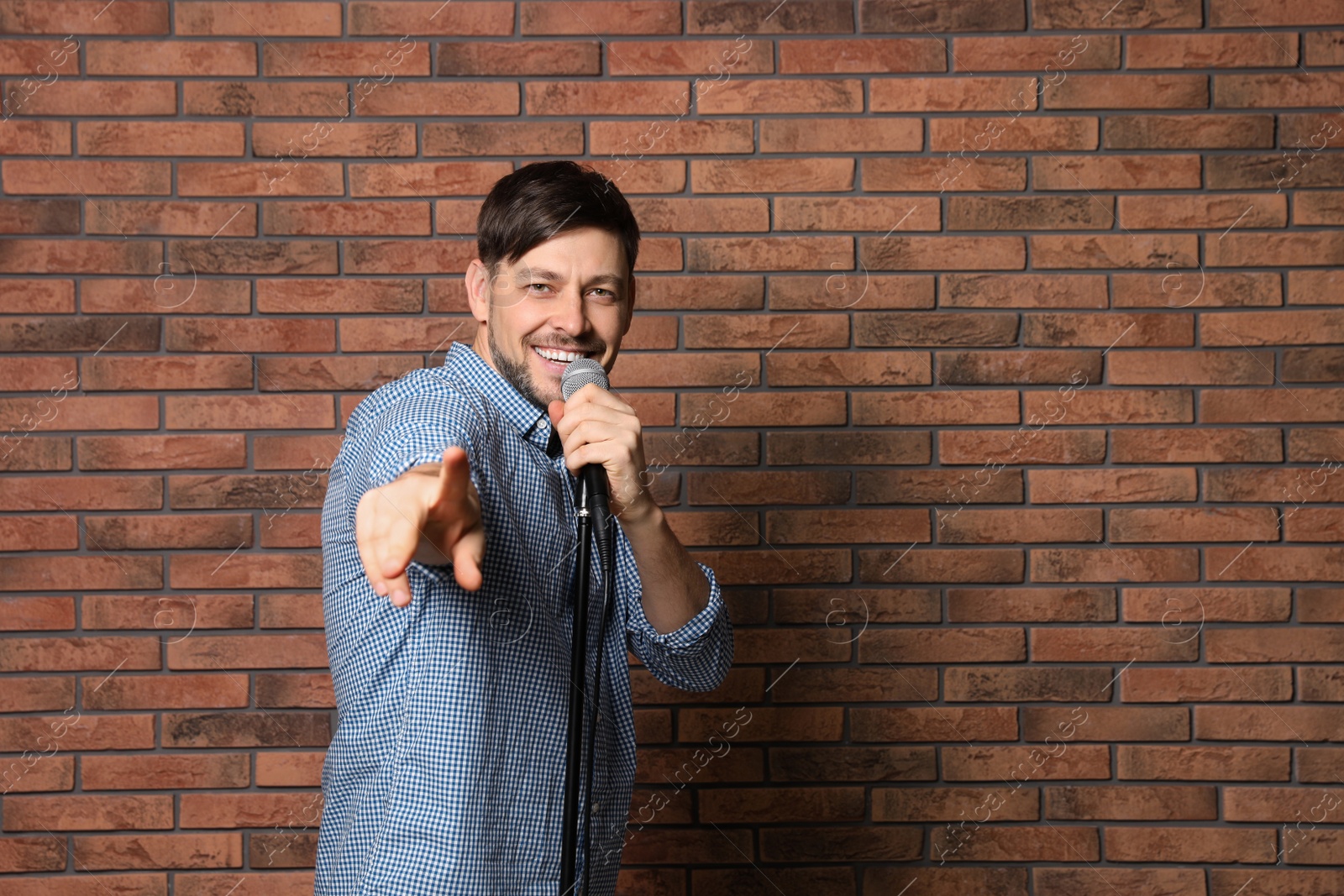 Photo of Handsome man in shirt singing with microphone near brick wall. Space for text