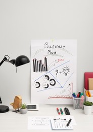 Photo of Business process planning and optimization. Workplace with plan, lamp, notebook and stationery on white wooden table