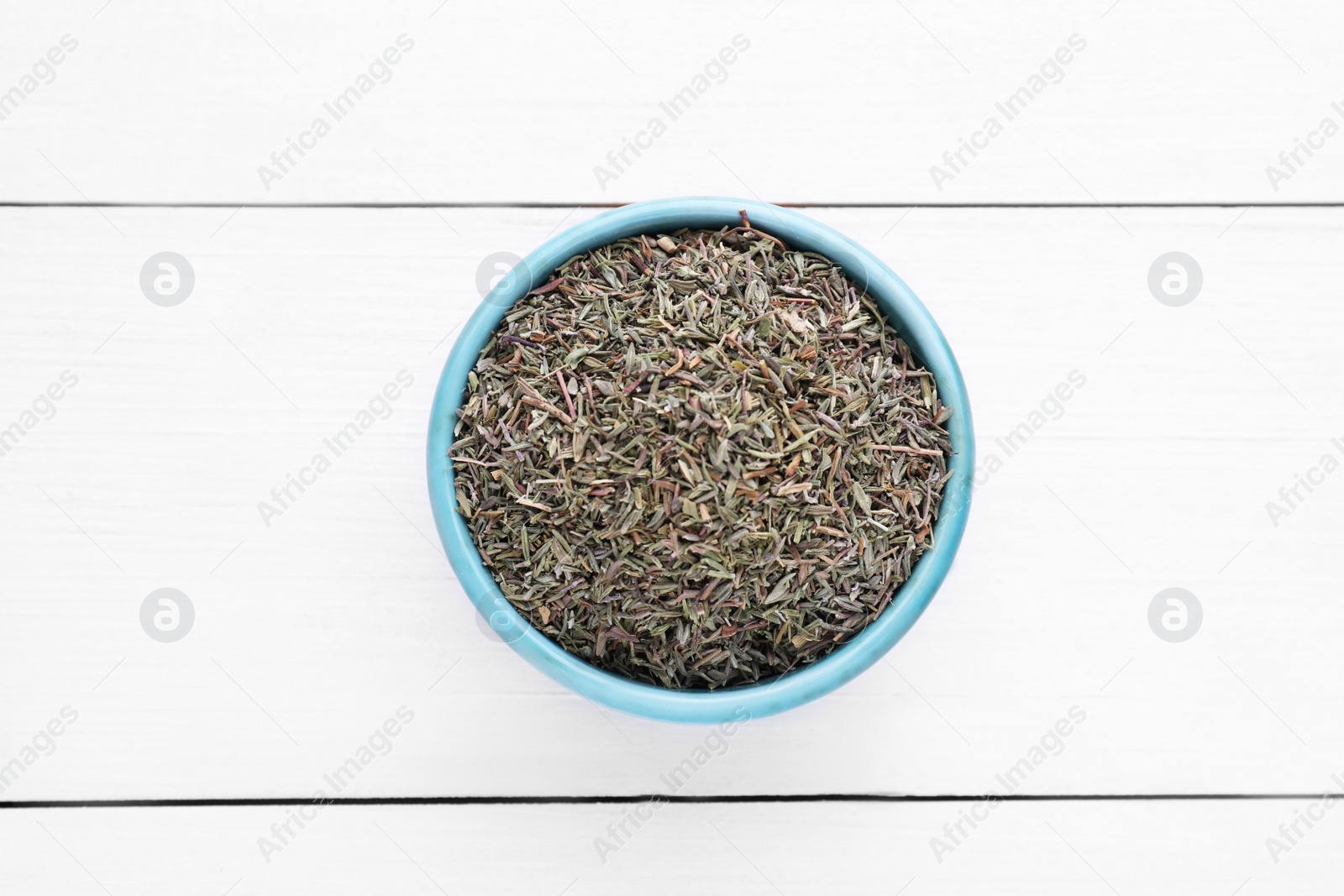Photo of Ceramic bowl with dried thyme on white wooden table, top view