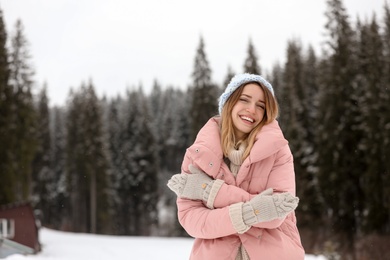 Photo of Young woman in warm clothes near forest, space for text. Winter vacation
