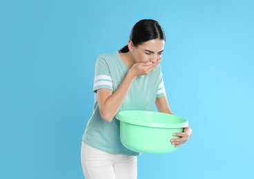 Woman with basin suffering from nausea on light blue background. Food poisoning