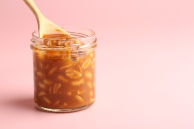 Taking tasty salted caramel with peanuts from jar on pink background, closeup. Space for text