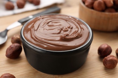 Photo of Bowl with delicious chocolate paste and nuts on wooden table, closeup