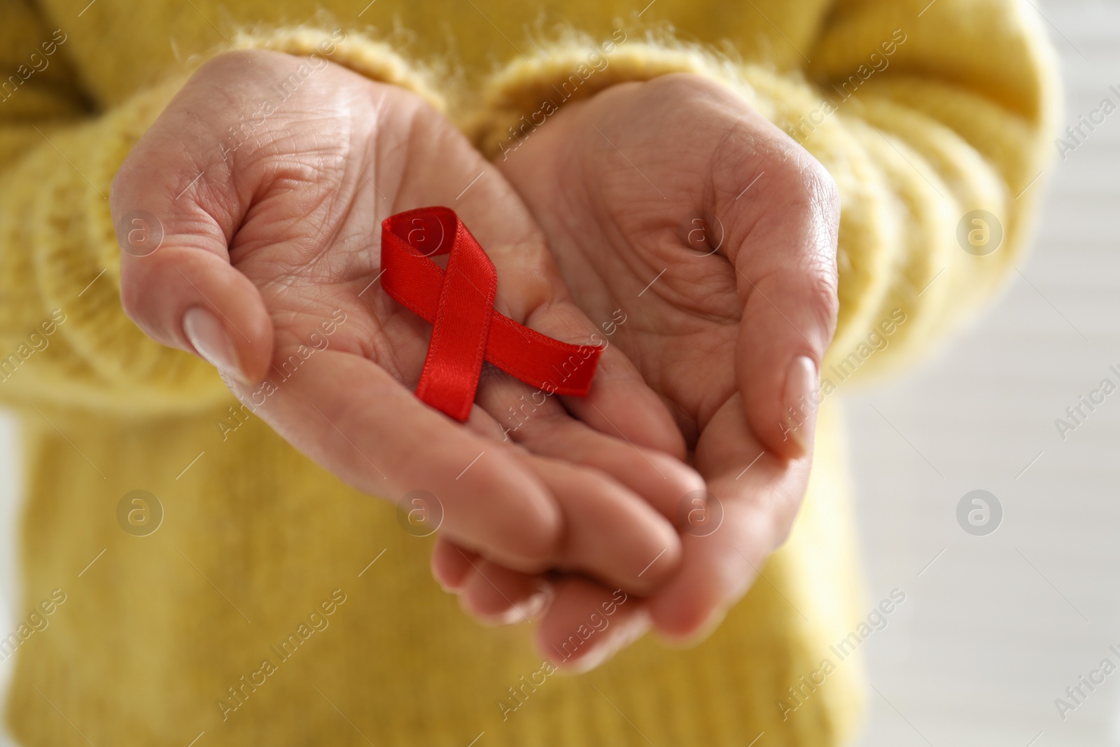 Photo of Woman holding red awareness ribbon on light background, closeup. World AIDS disease day