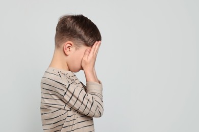 Boy covering face with hands on light grey background, space for text. Children's bullying
