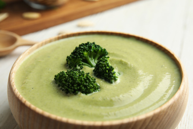 Photo of Wooden bowl of delicious broccoli cream soup on table, closeup