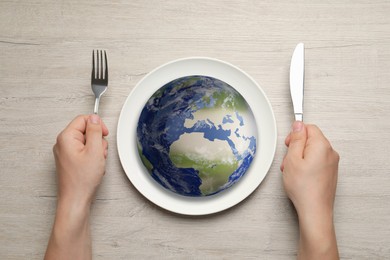 Image of Global food crisis concept. Man with cutlery and globe of Earth in plate at wooden table, top view