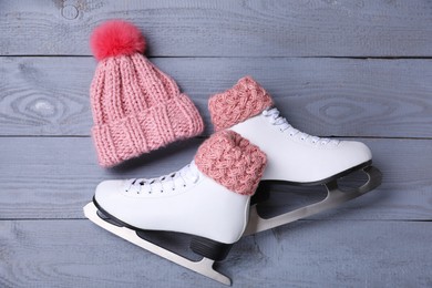 Pair of ice skates and knitted hat on grey wooden background, flat lay