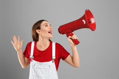 Emotional young woman with megaphone on light grey background