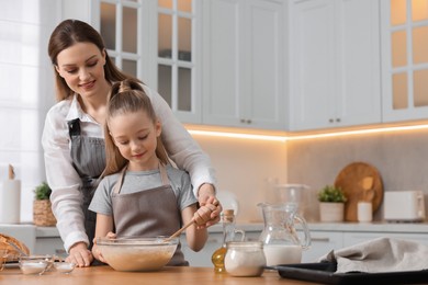 Photo of Making bread. Mother and her daughter preparing dough in bowl at wooden table in kitchen