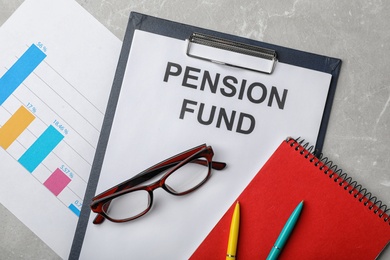 Photo of Stationery, glasses, notebook, chart and paper with words PENSION FUND on table, flat lay