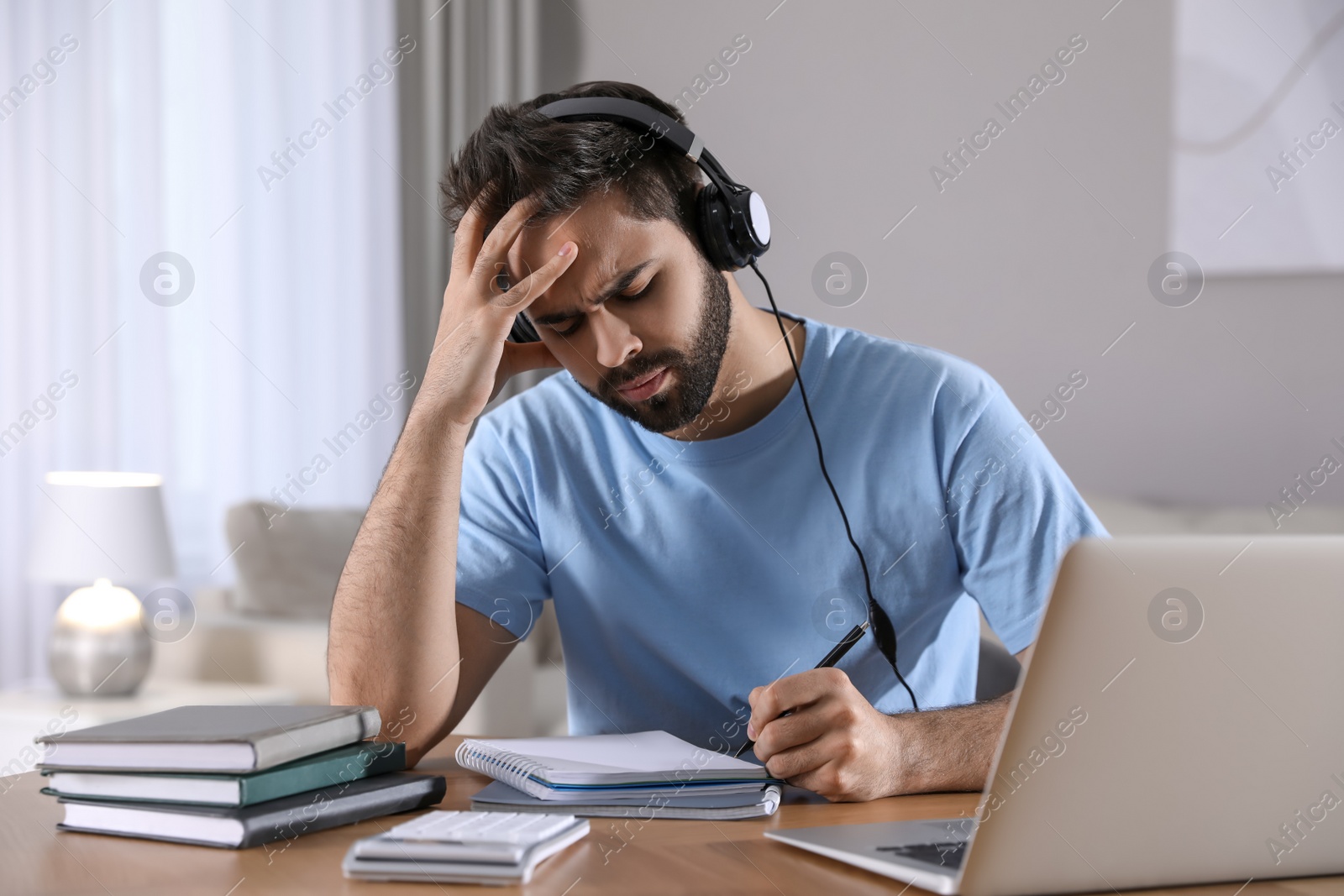 Photo of Confused young man writing down notes during webinar at table in room