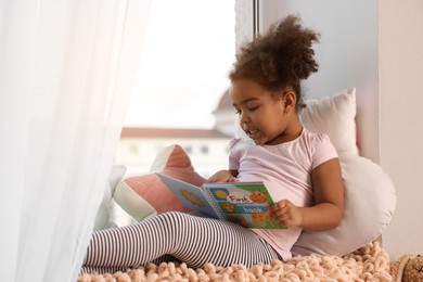 Photo of African American girl reading book at home