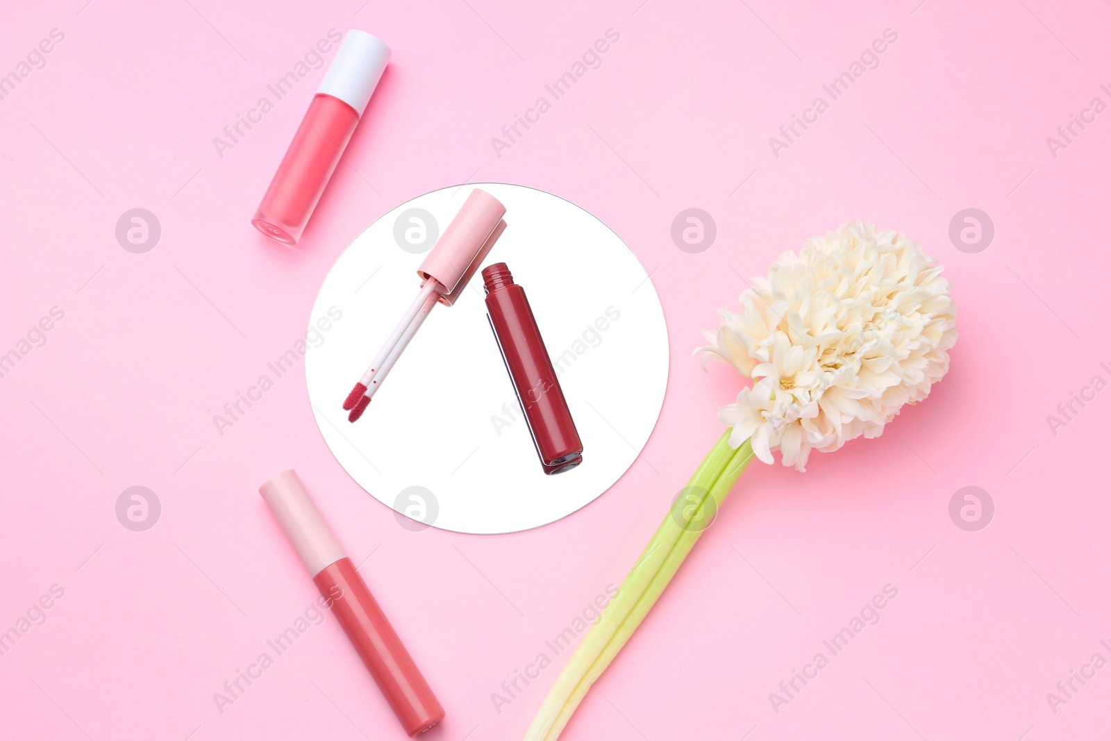 Photo of Different lip glosses, hyacinth and mirror on pink background, flat lay