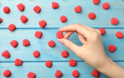 Photo of Woman taking delicious gummy raspberry candy at light blue wooden table, top view