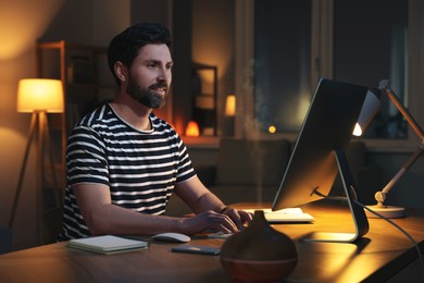Photo of Home workplace. Man working with computer at wooden desk in room at night