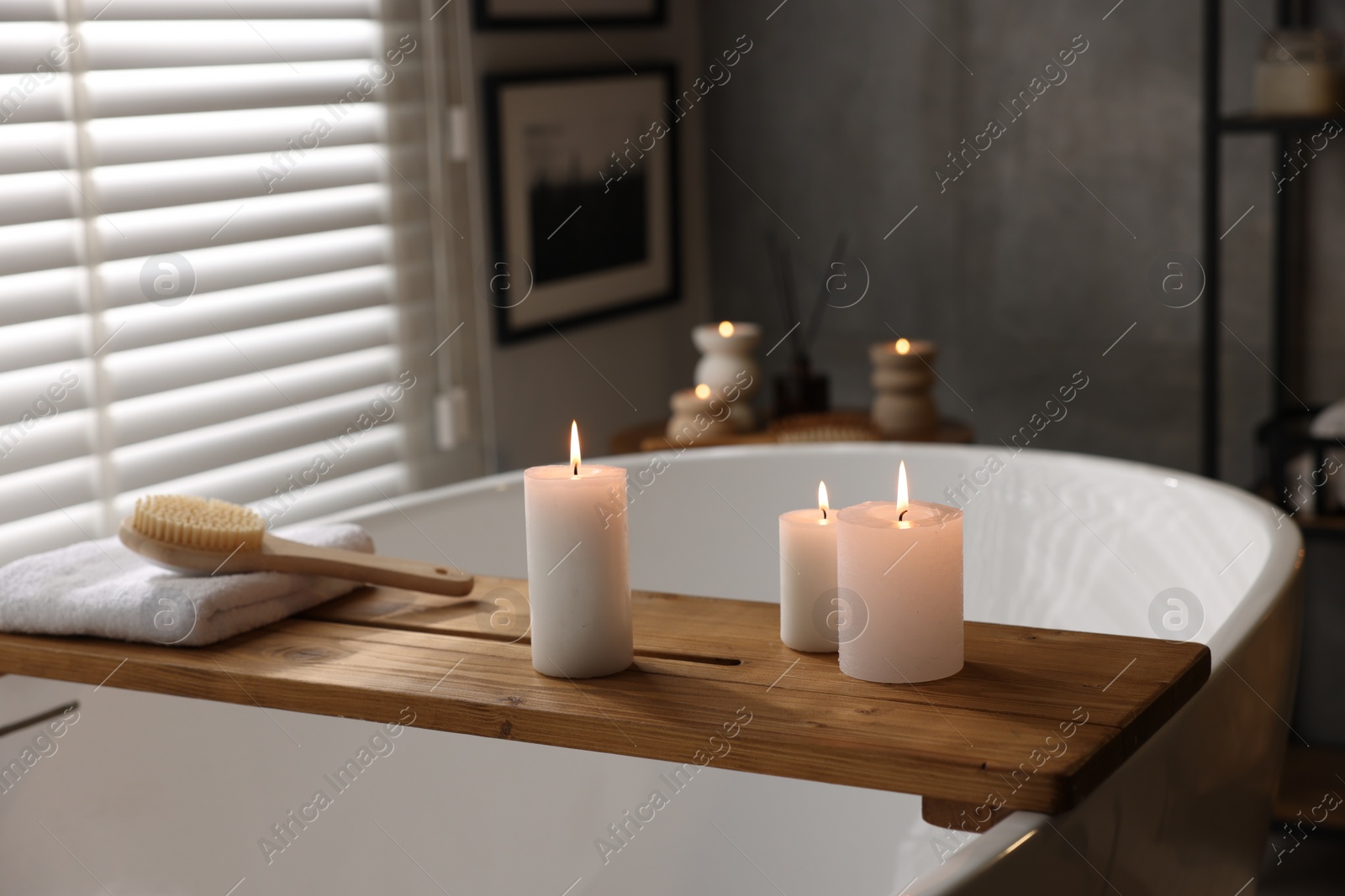 Photo of Wooden tray with burning candles, towel and brush on bathtub in bathroom