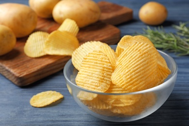 Photo of Bowl of crispy potato chips on wooden table. Space for text