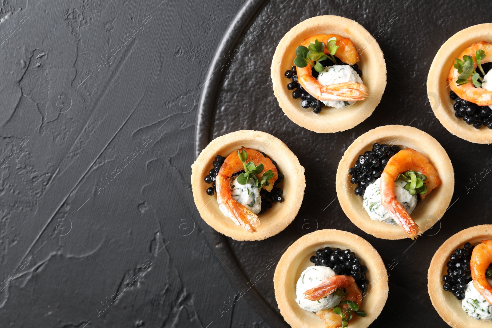 Photo of Delicious canapes with shrimps and black caviar on black textured table, top view. Space for text