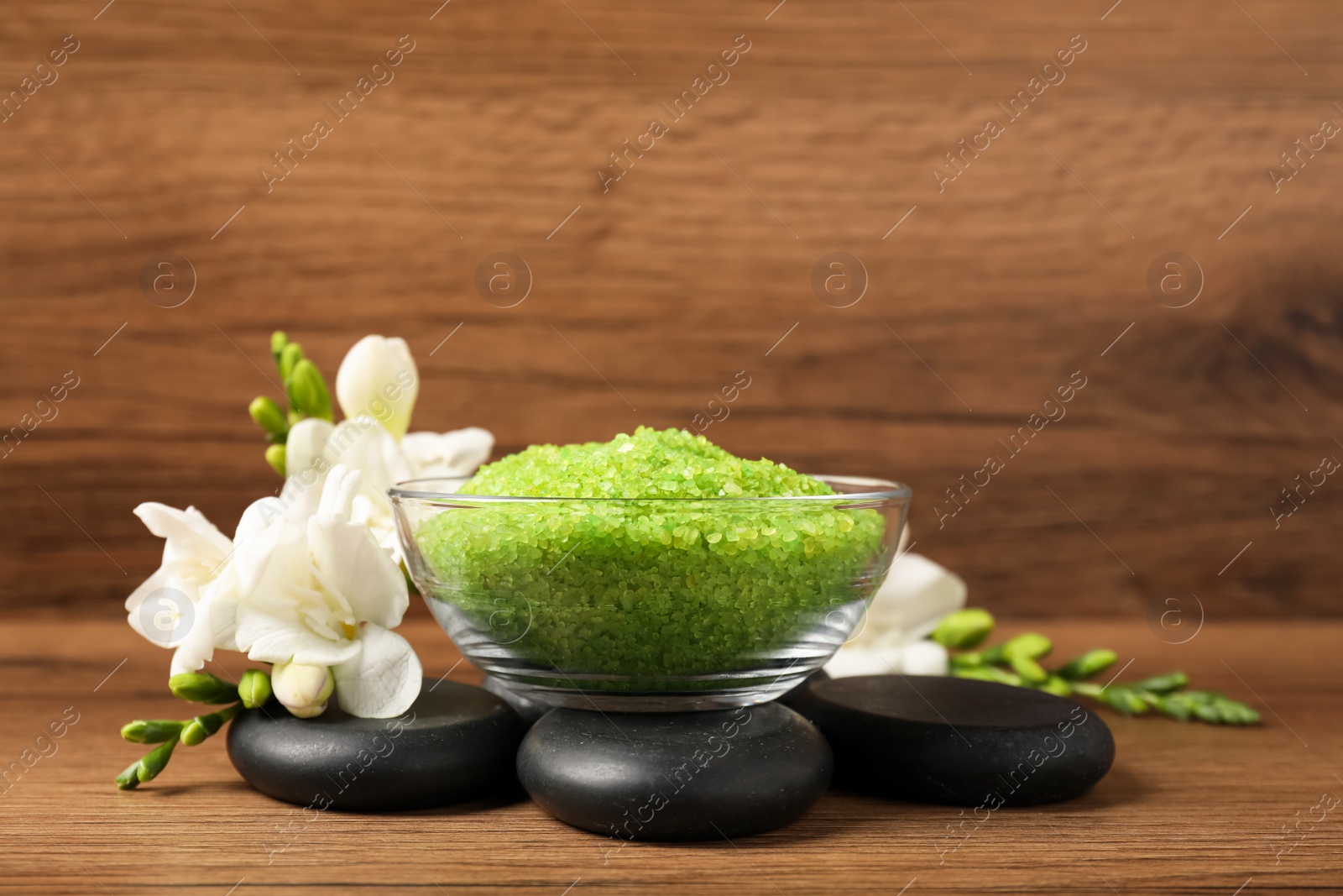 Photo of Aromatic sea salt, flowers and spa stones on wooden table, space for text