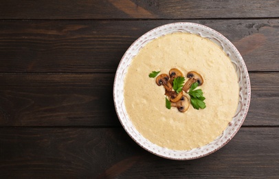 Bowl of fresh homemade mushroom soup on wooden background, top view with space for text