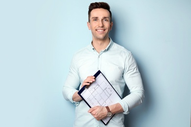 Male real estate agent with clipboard on light background