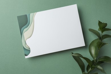 Blank invitation card and branch on green background, top view. Space for text