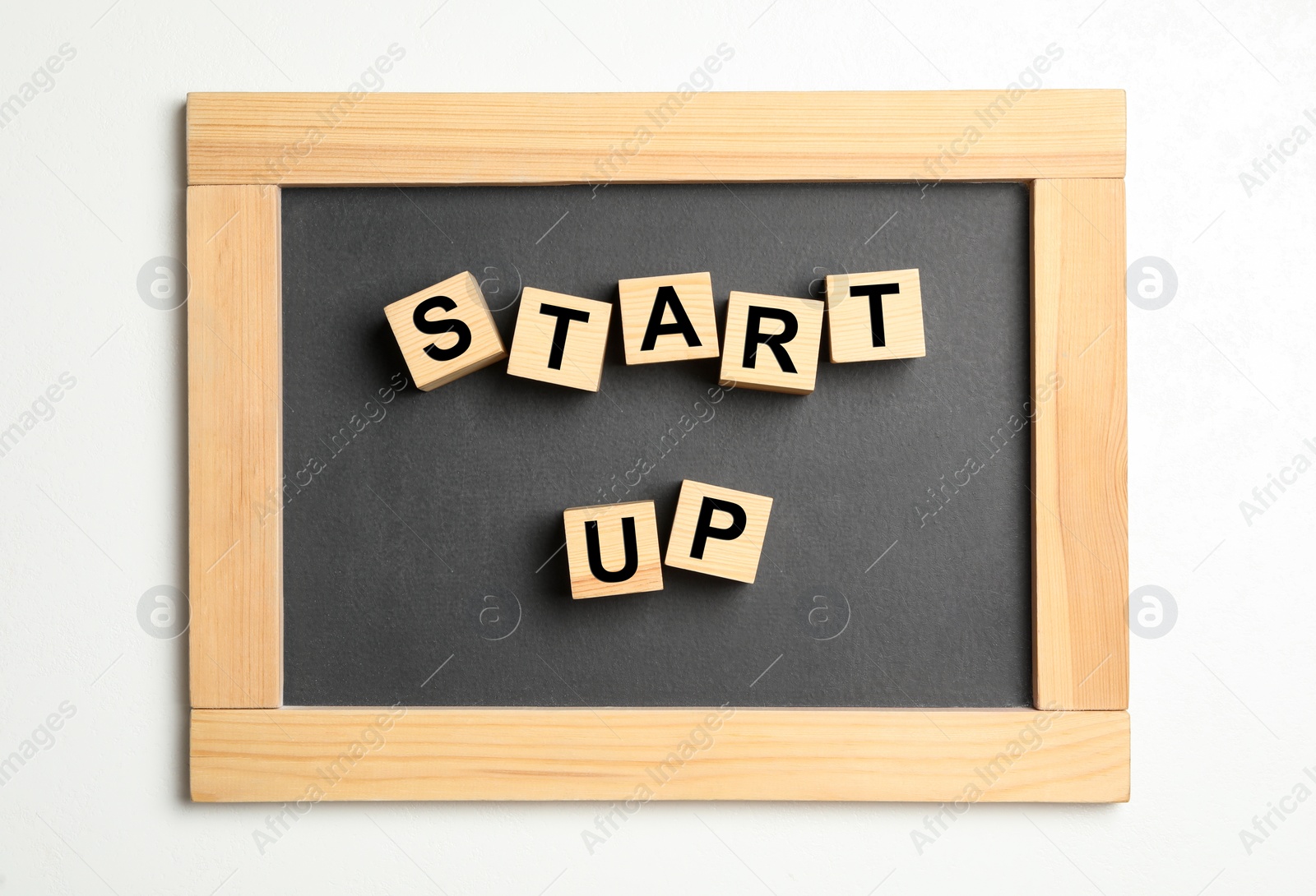 Photo of Words START UP made with wooden cubes and chalkboard on white background, top view