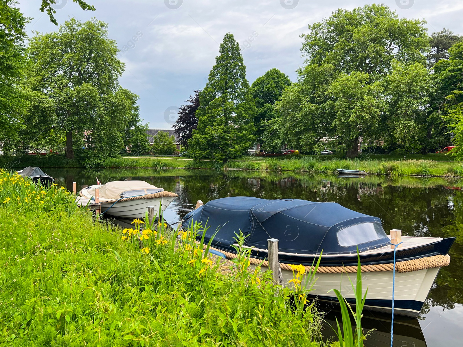 Photo of Beautiful view of city canal with moored boats surrounded by greenery