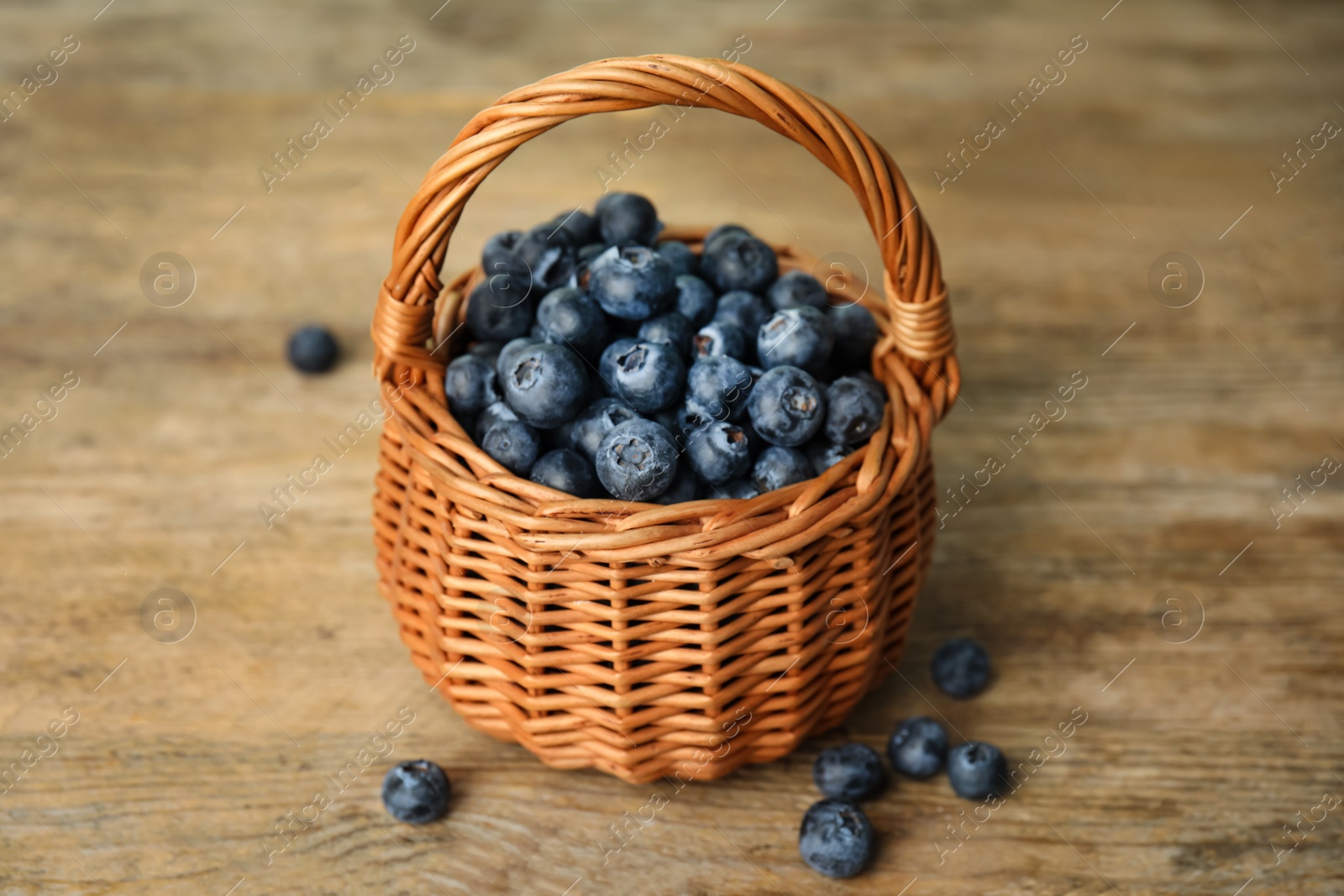 Photo of Tasty ripe blueberries in wicker basket on wooden table