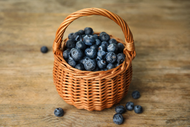 Photo of Tasty ripe blueberries in wicker basket on wooden table