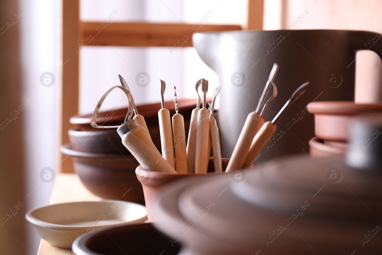 Photo of Set of different crafting tools and clay dishes on table in workshop, closeup