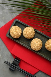 Photo of Delicious sesame balls, green leaf and chopsticks on grey table, flat lay