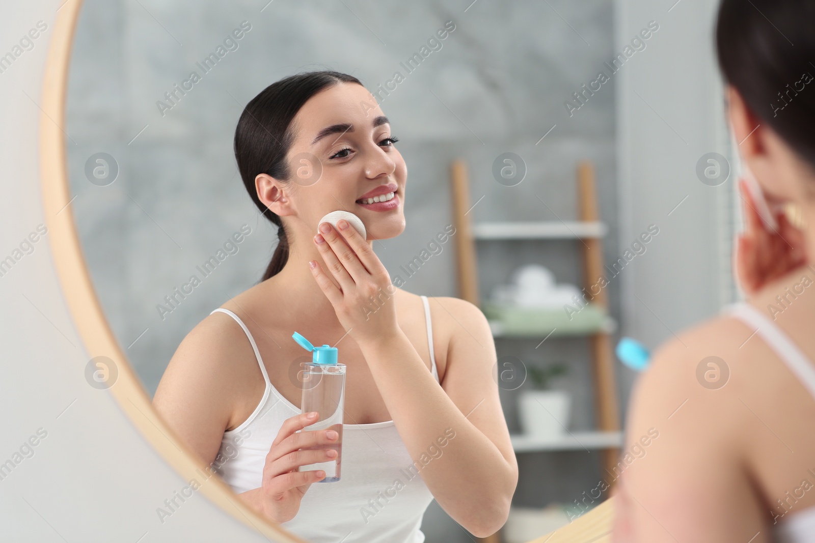 Photo of Beautiful woman removing makeup with cotton pad near mirror indoors