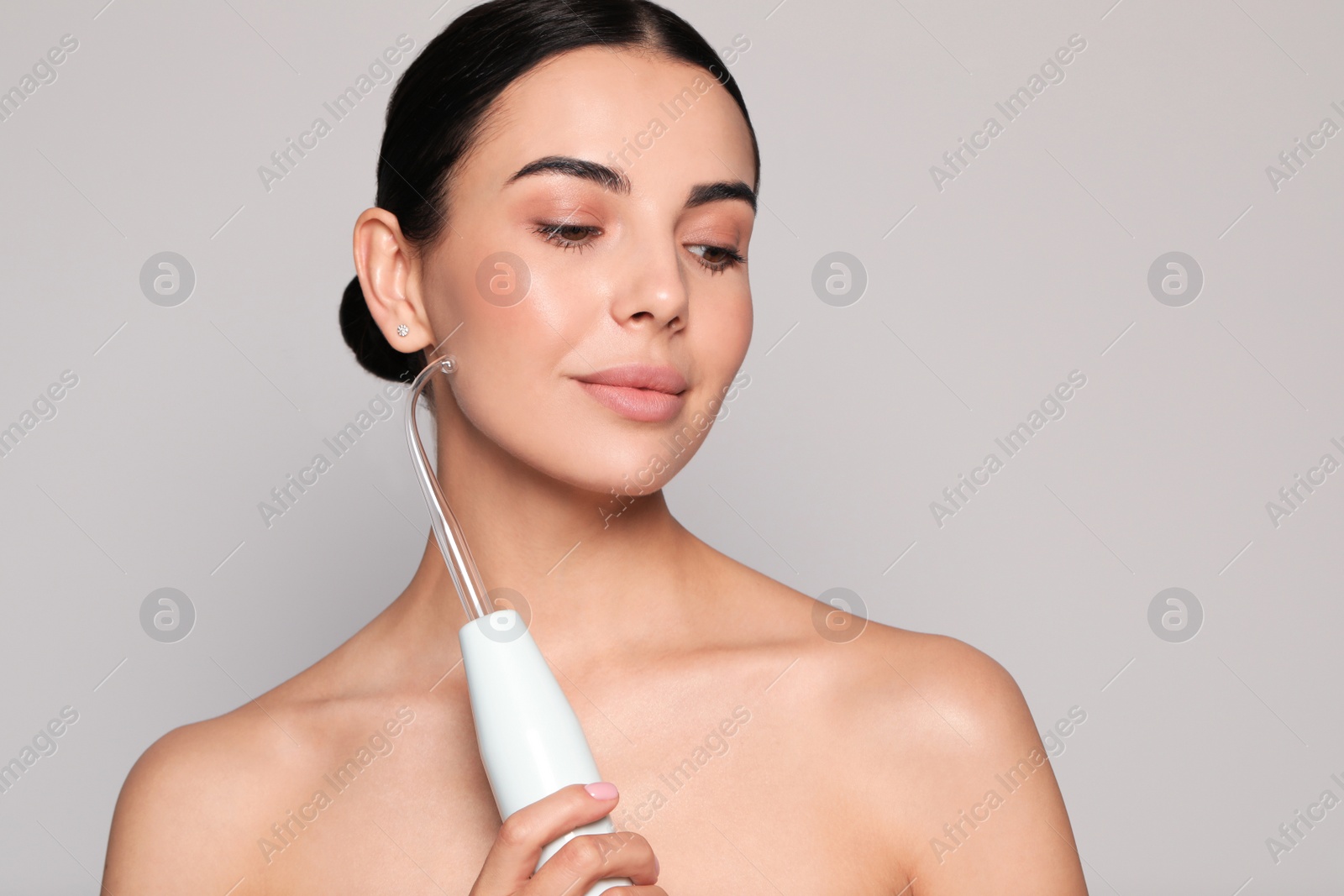 Photo of Woman using high frequency darsonval device on grey background. Space for text