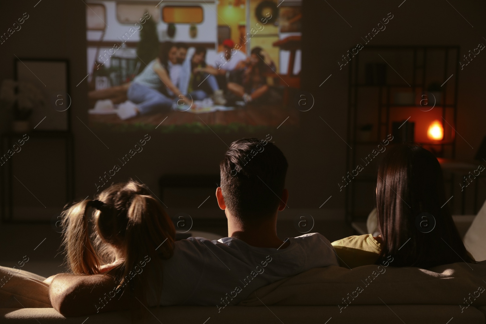 Photo of Family watching movie on sofa at night, back view