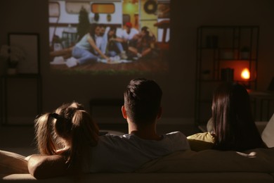 Family watching movie on sofa at night, back view