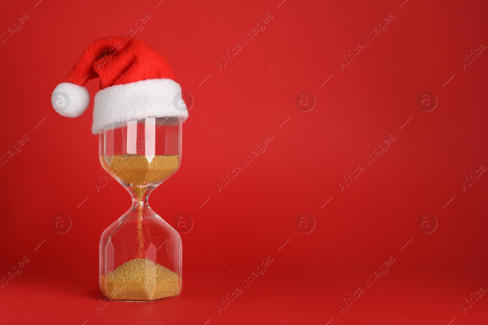 Photo of Hourglass and Santa hat on red background, space for text. Christmas countdown