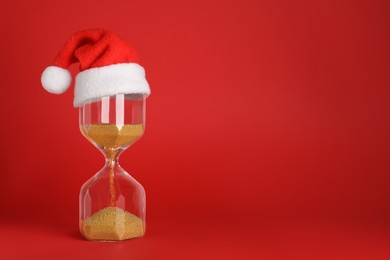 Photo of Hourglass and Santa hat on red background, space for text. Christmas countdown