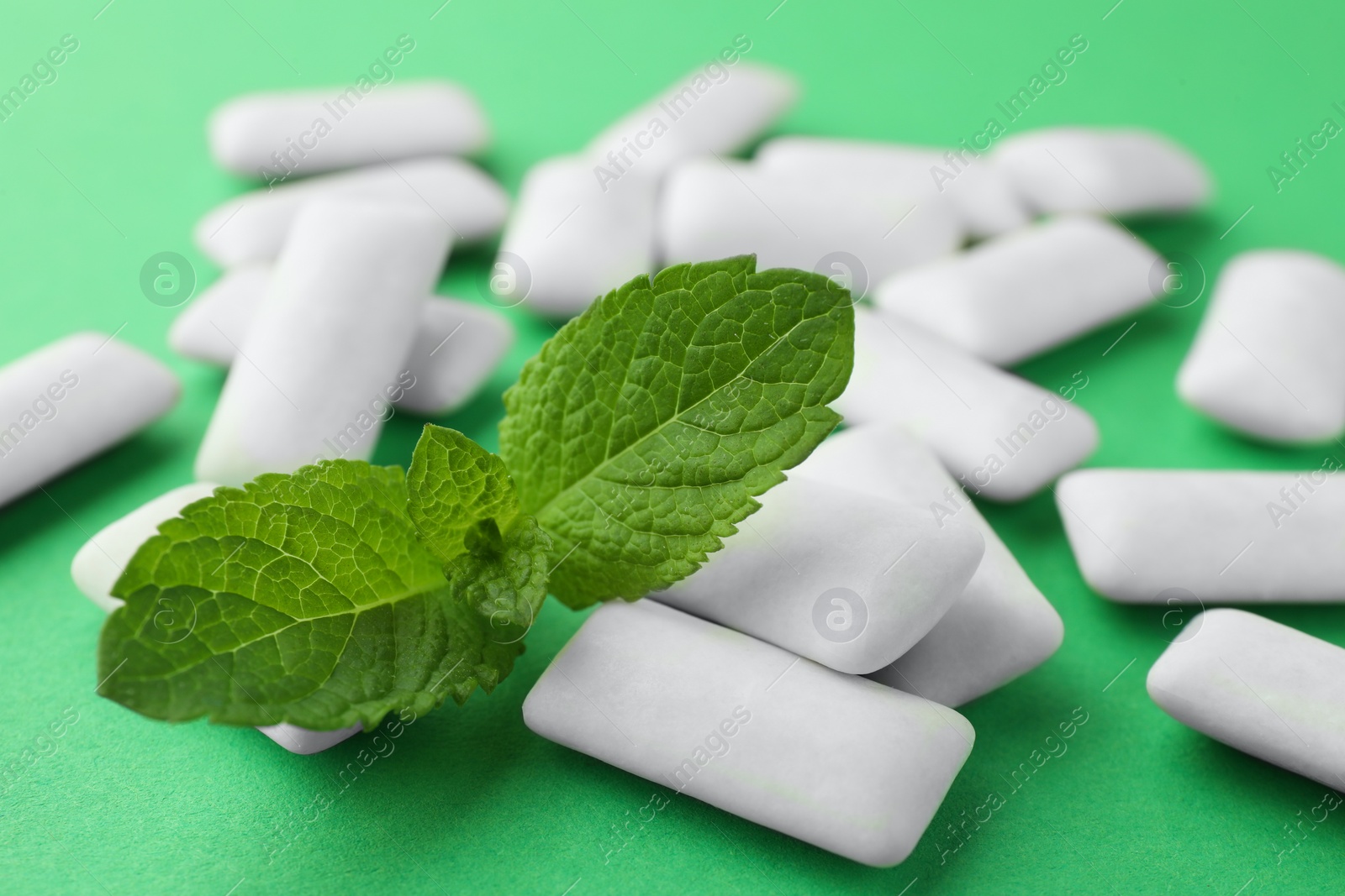 Photo of Tasty white chewing gums and mint leaves on green background, closeup