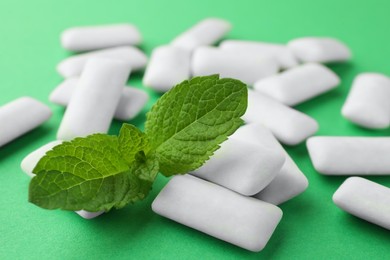 Tasty white chewing gums and mint leaves on green background, closeup
