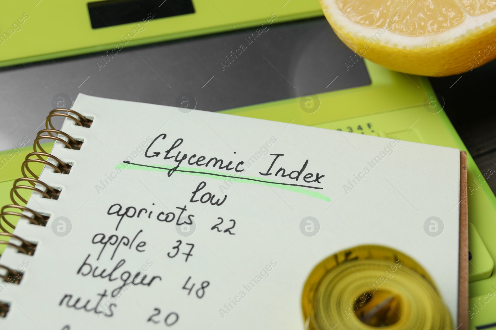 Photo of Notebook with products of low glycemic index, calculator, measuring tape and lemon, closeup