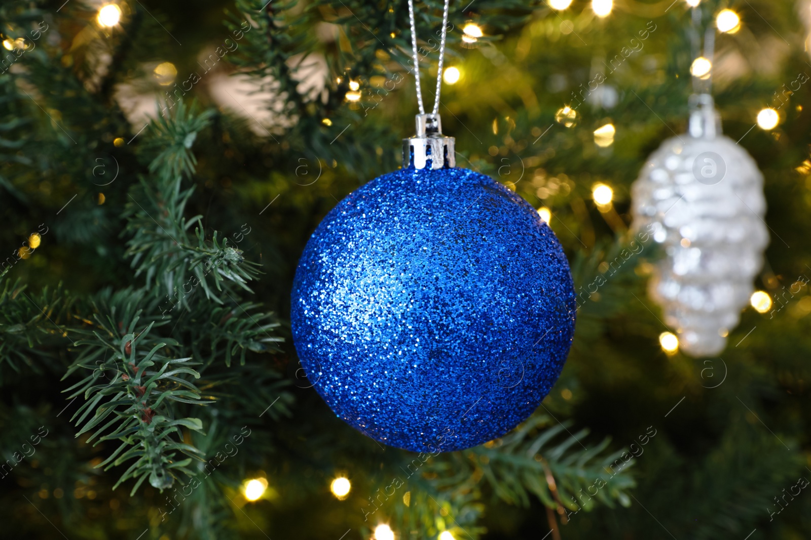 Photo of Beautiful blue Christmas ball hanging on fir tree branch, closeup