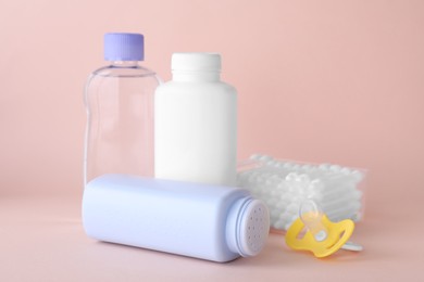 Photo of Different skin care products for baby, cotton buds and pacifier on light coral background. Space for text
