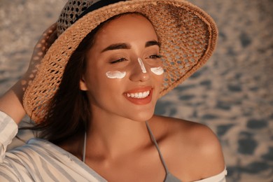 Photo of Happy young woman with sun protection cream on face at beach