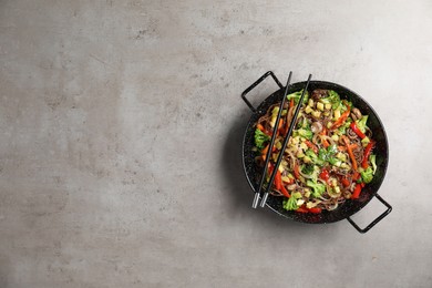 Photo of Stir-fry. Tasty noodles with meat in wok and chopsticks on grey textured table, top view. Space for text