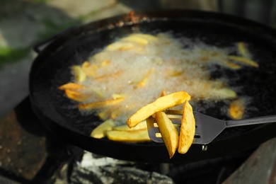 Photo of Cooking delicious potato wedges on frying pan outdoors